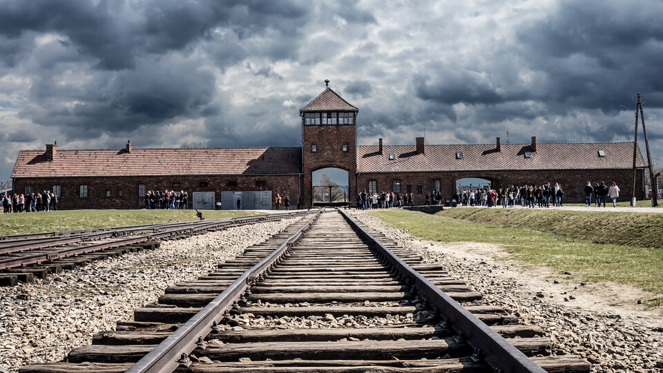 Photo Credit: Visitors gather near the gate rail entrance, of Auschwitz Birkenau, a Nazi concentration and extermination camp in Poland.